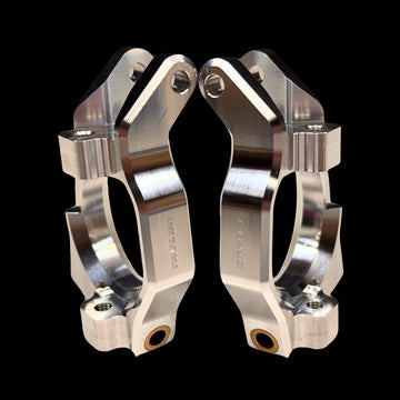A pair of silver billet spindle carriers for RC cars, showing intricate machining and black hardware.