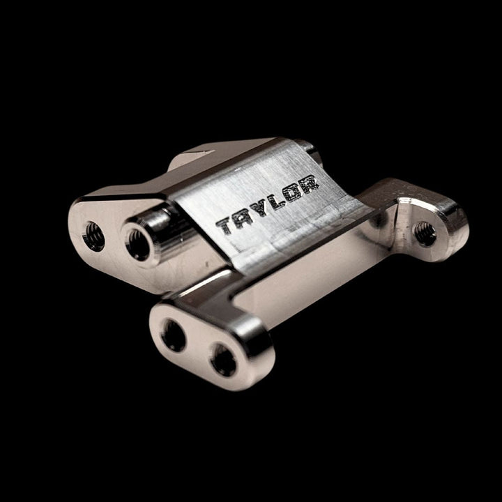 A silver billet front suspension mount with the brand name 'Taylor' engraved on it.
